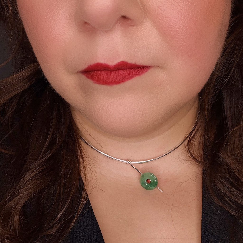 A close-up of a person's lower face and neck wearing a delicate silver wire choker necklace with a small green circular pendant.