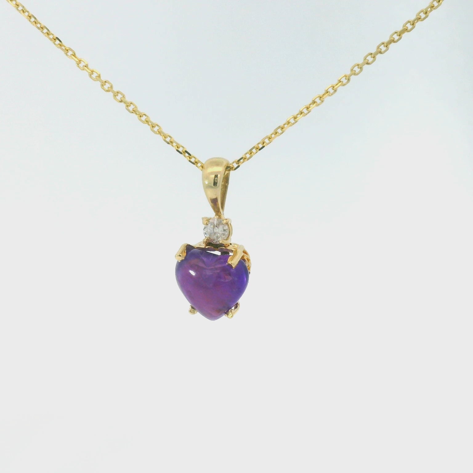 Video of a Gold necklace with a heart-shaped purple gemstone pendant on a white background spinning 360 degrees.